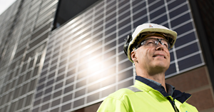 Pertti Vanhala stands infornt of a solar panel wall of Toppila power plant. 