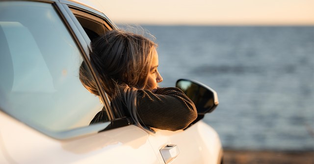 A young woman leans out of a car window on a summer evening. Bay of Bothnia can be seen in the background.