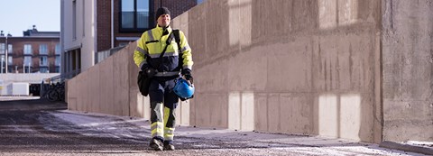 An employee of Oulu Energy is walking in his work gear in front of a building.