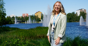 HR:n kesätyöntekijä Aino Saniola seisoo Ainolanpuistossa. Taustalla näkyy Toivoniemi ja kauneusaltaan suihkulähteet. 