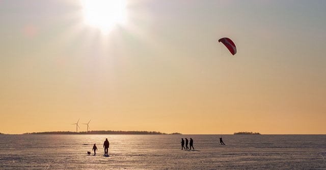  People are walking on the icy sea. Two wind turbines behind.