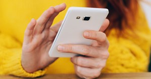 A red-haired woman wearing a yellow sweater browses through her white smartphone.