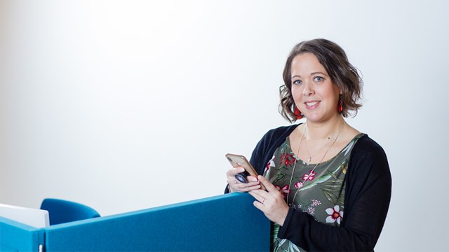 An Oulun Energia employee poses in the office with a smartphone in hand.